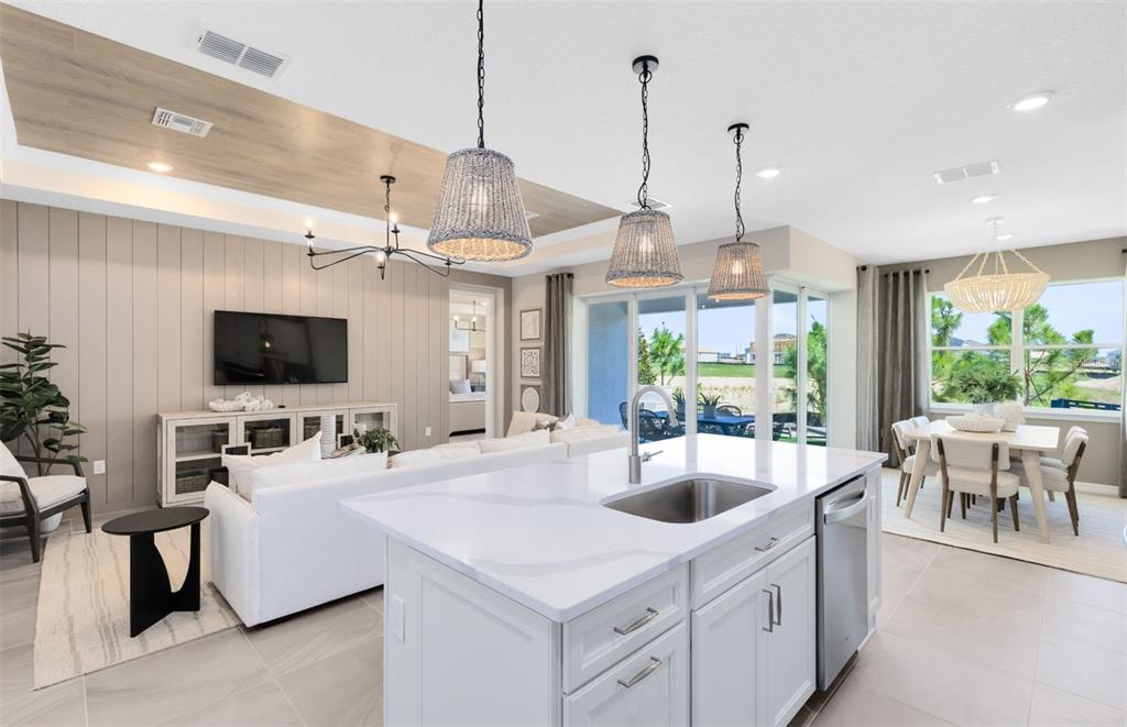 A modern open-concept kitchen and living area featuring white cabinetry, quartz countertops, and wood accents — 33387 BARNEBROOK DRIVE, WESLEY CHAPEL, FL