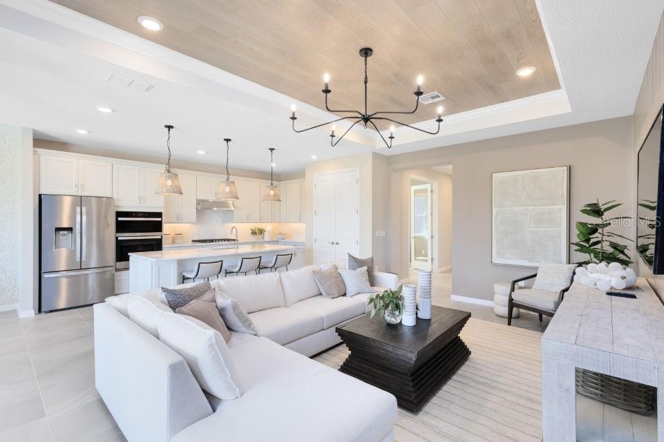 An open-concept living room and kitchen featuring a tray ceiling, chandelier, and white cabinetry — 33387 BARNEBROOK DRIVE, WESLEY CHAPEL, FL