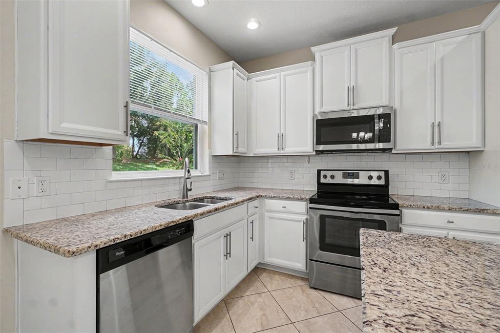 A kitchen with white cabinets, granite countertops, stainless steel appliances, and a subway tile backsplash — 12411 TRAILHEAD DRIVE, BRADENTON, FL