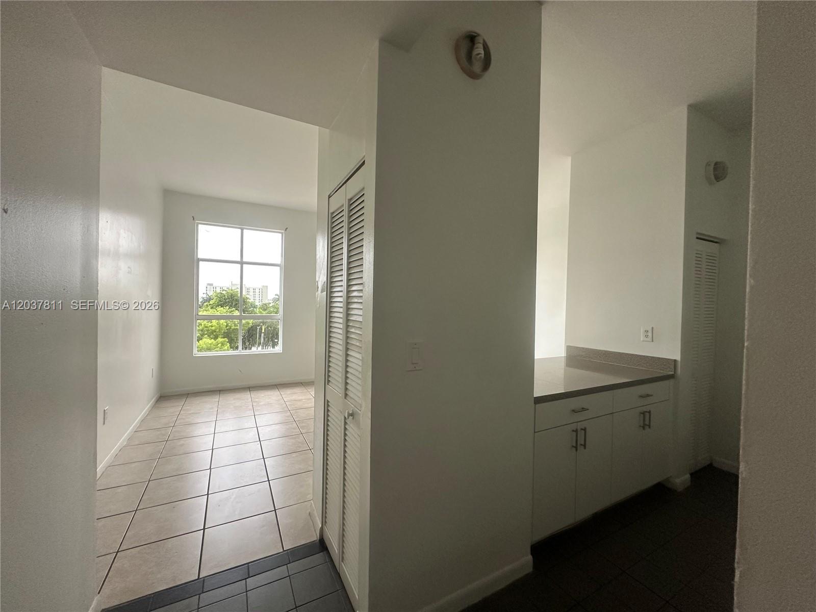 A view of a tiled room with a window and an adjacent kitchen counter area — 7420 W 20th Ave # 452, Hialeah FL 33016, HIALEAH, FL