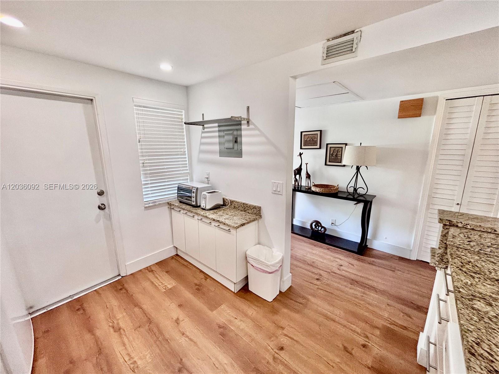 A kitchen area features white cabinets, granite countertops, wood-look flooring, and an adjacent entryway — 3051 S Palm Aire Dr # 102, Pompano Beach FL 33069, POMPANO BEACH, FL