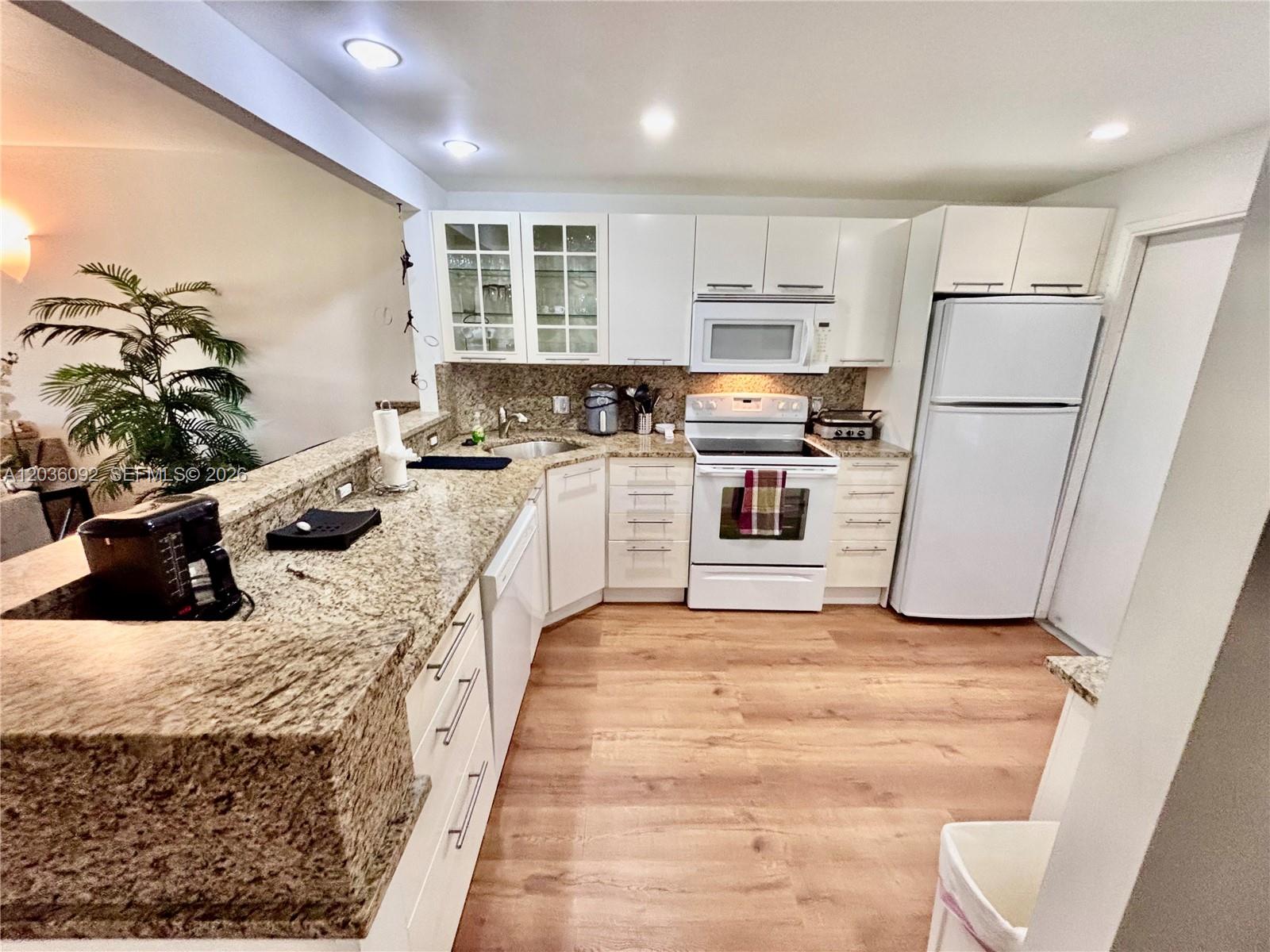 A kitchen features white cabinets, granite countertops, stainless steel appliances, and light wood flooring — 3051 S Palm Aire Dr # 102, Pompano Beach FL 33069, POMPANO BEACH, FL