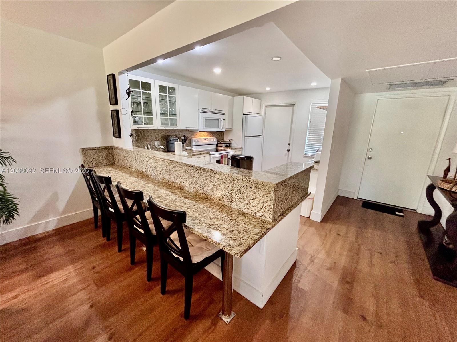 A kitchen features granite countertops, white cabinetry, and a breakfast bar with four chairs — 3051 S Palm Aire Dr # 102, Pompano Beach FL 33069, POMPANO BEACH, FL