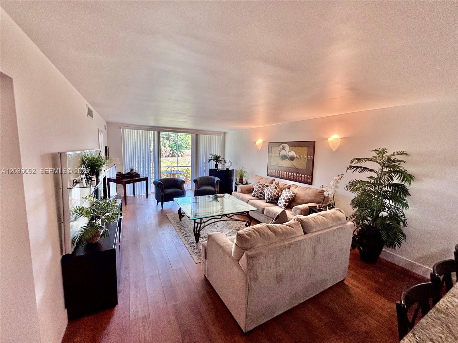 A living room features a beige sofa, glass coffee table, wood flooring, and a sliding door — 3051 S Palm Aire Dr # 102, Pompano Beach FL 33069, POMPANO BEACH, FL