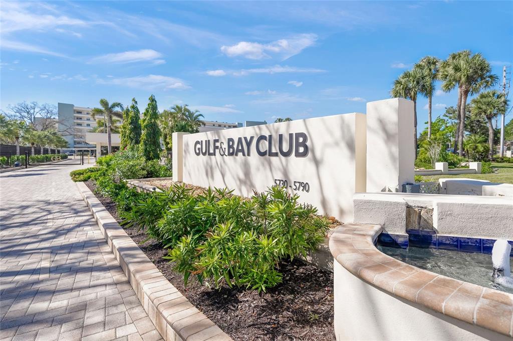 A stone sign for Gulf & Bay Club stands beside a fountain and paved walkway — 5780 MIDNIGHT PASS ROAD UNIT B105, SARASOTA, FL