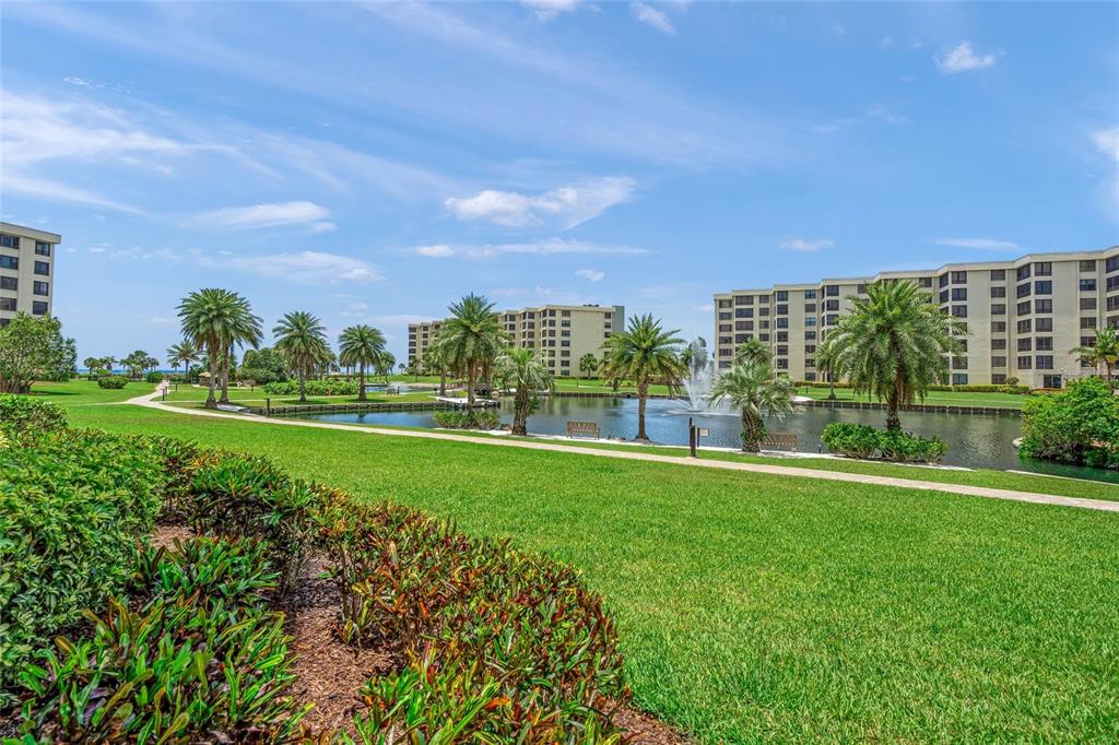 A grassy lawn leads to a pond with a fountain and multi-story apartment buildings — 5780 MIDNIGHT PASS ROAD UNIT B105, SARASOTA, FL