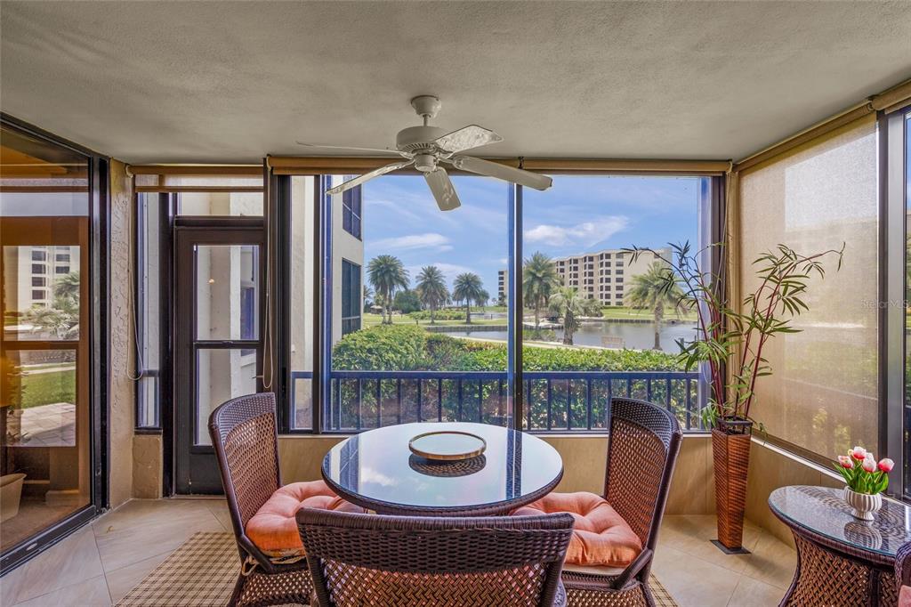 A screened-in patio features wicker furniture, a ceiling fan, and a view of a lake — 5780 MIDNIGHT PASS ROAD UNIT B105, SARASOTA, FL
