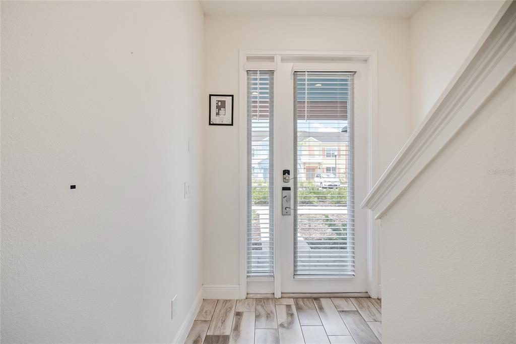 An entryway with wood-look tile flooring, a glass-paneled door, and a staircase railing — 2915 CASTAWAY LANE, KISSIMMEE, FL
