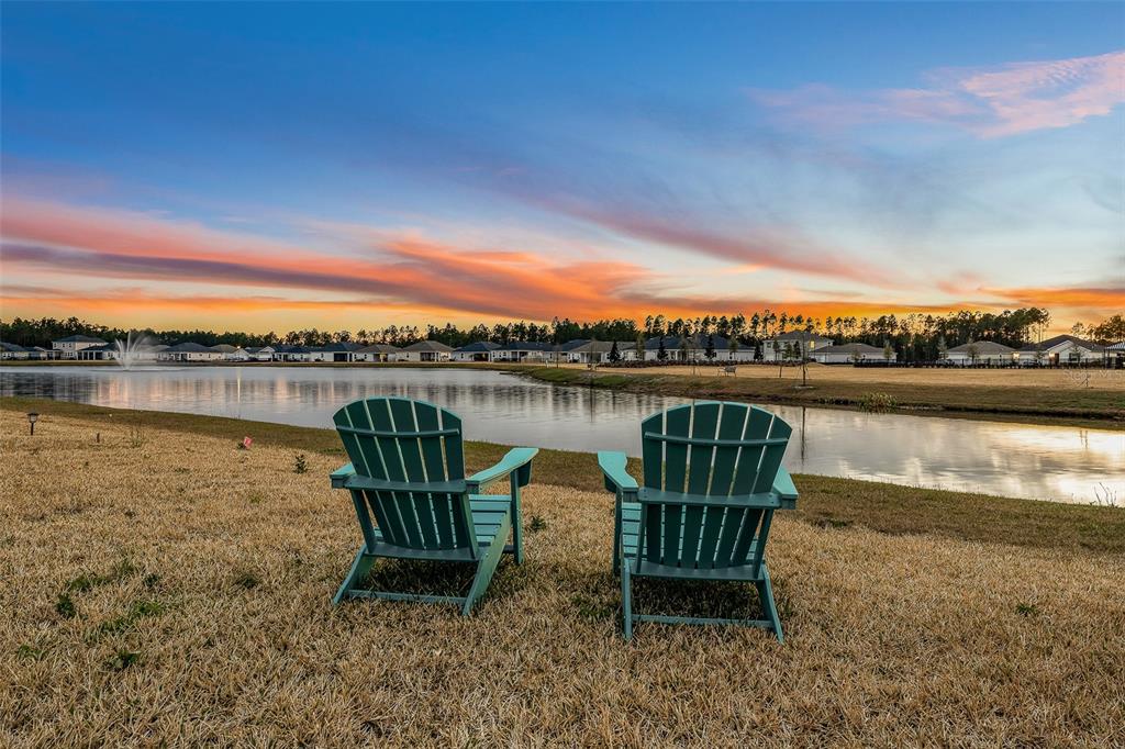 Two teal Adirondack chairs sit on a grassy lawn overlooking a pond at sunset — 55 CAMELLIA STREET, PALM COAST, FL