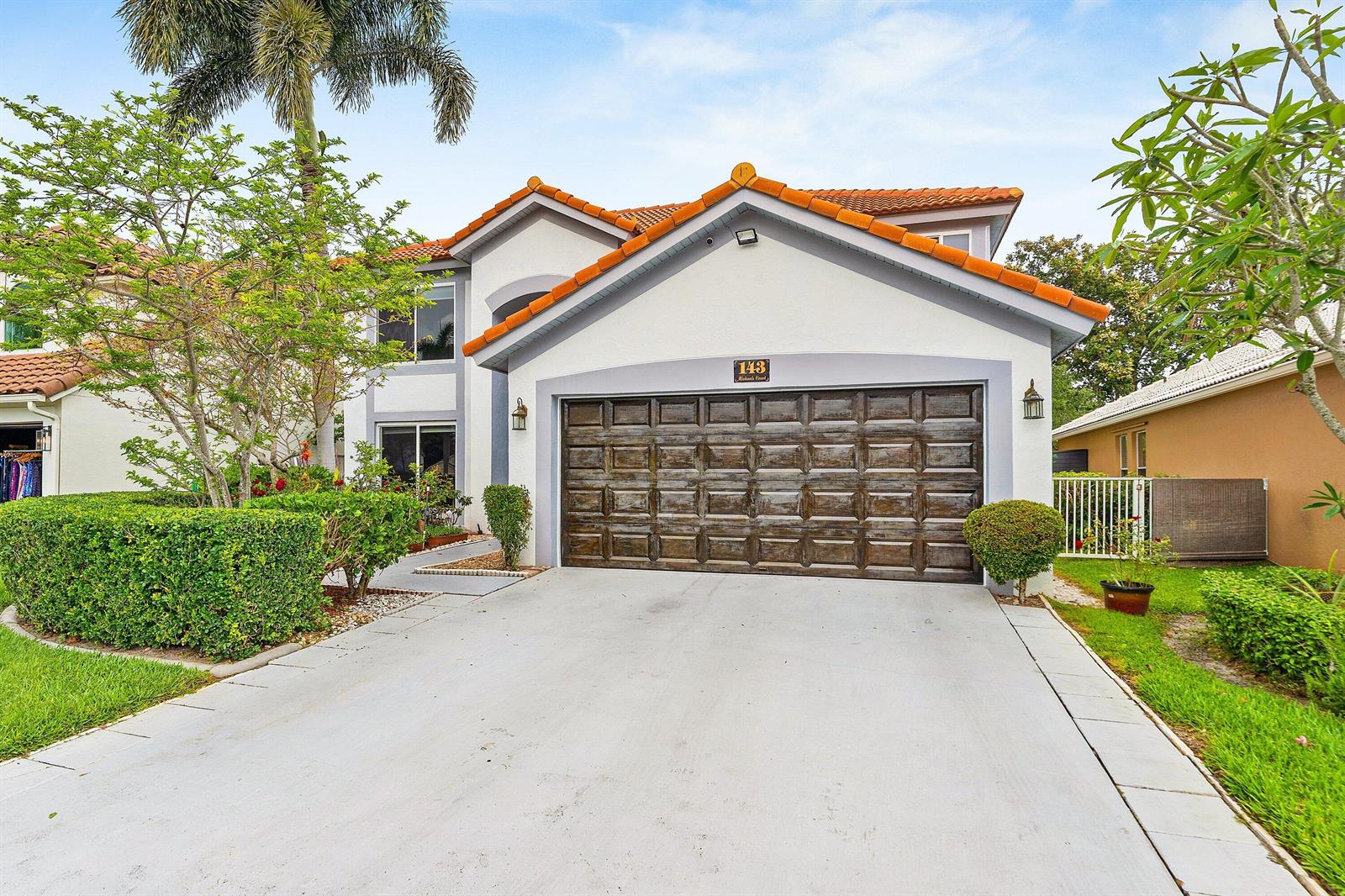 A two-story house features a brown garage door, white stucco walls, and orange roof tiles — 143 St Michaels Court, Jupiter FL 33458, JUPITER, FL