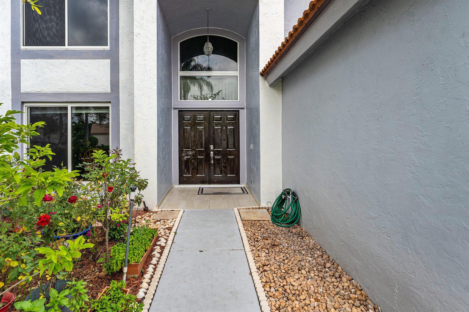 A concrete walkway leads to the dark double front doors of a two-story stucco house — 143 St Michaels Court, Jupiter FL 33458, JUPITER, FL