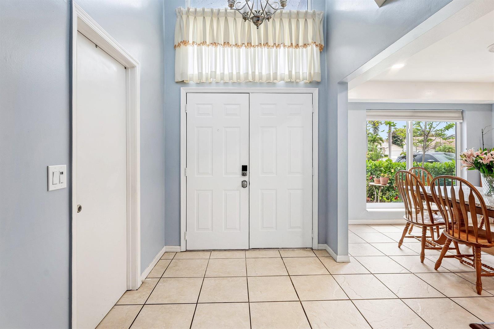 A foyer with light blue walls, tile flooring, and double front doors under a chandelier — 143 St Michaels Court, Jupiter FL 33458, JUPITER, FL