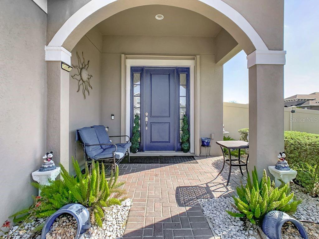 A covered front porch features a blue door, brick pavers, and potted plants — 200 TRINITY RIDGE CIRCLE, DAVENPORT, FL