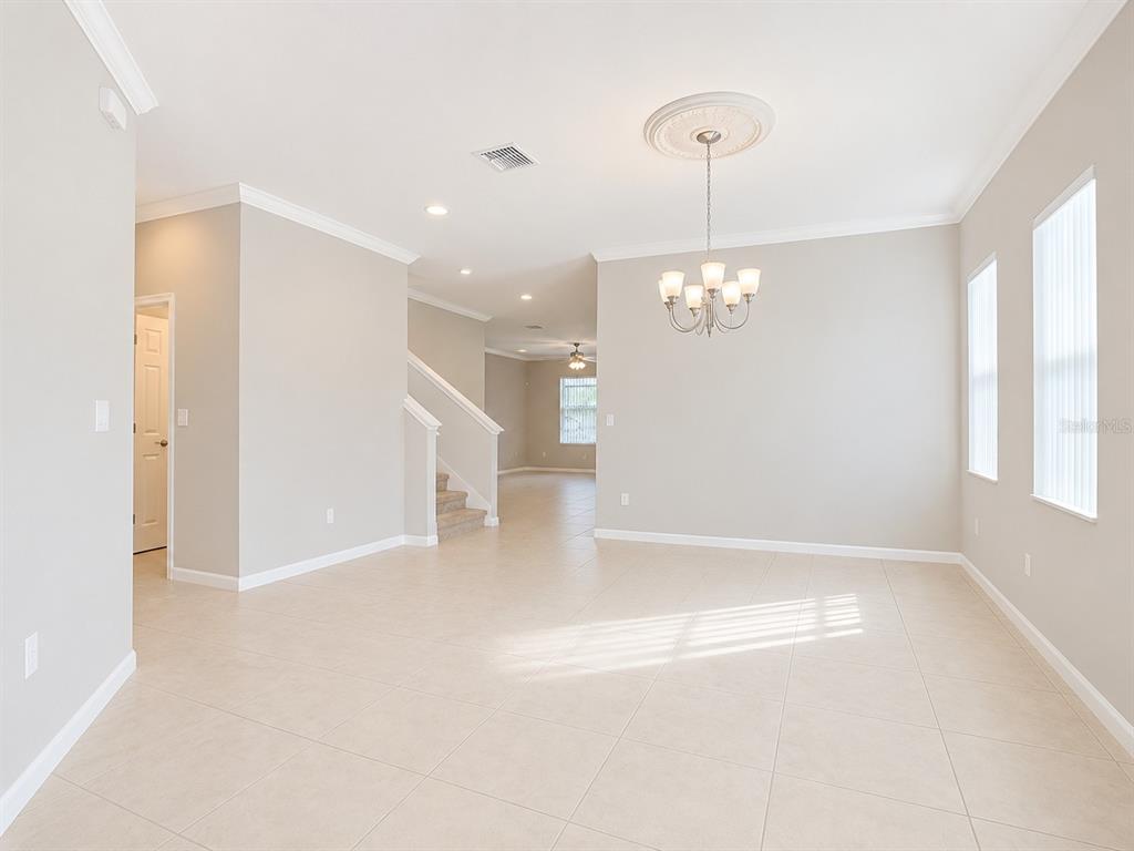 An open-concept dining area features tile flooring, a chandelier, and a staircase in the background — 200 TRINITY RIDGE CIRCLE, DAVENPORT, FL