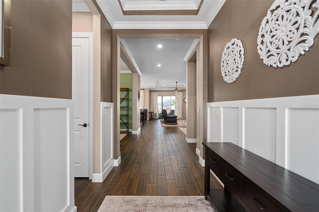A hallway with white wainscoting, brown walls, and wood-look tile flooring leads to a living area — 1357 ZEEK RIDGE STREET, CLERMONT, FL