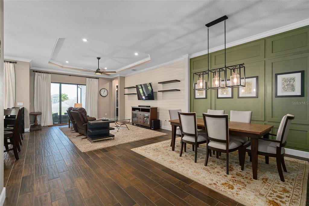 An open-concept living and dining area features wood-look tile floors and a green paneled wall — 1357 ZEEK RIDGE STREET, CLERMONT, FL