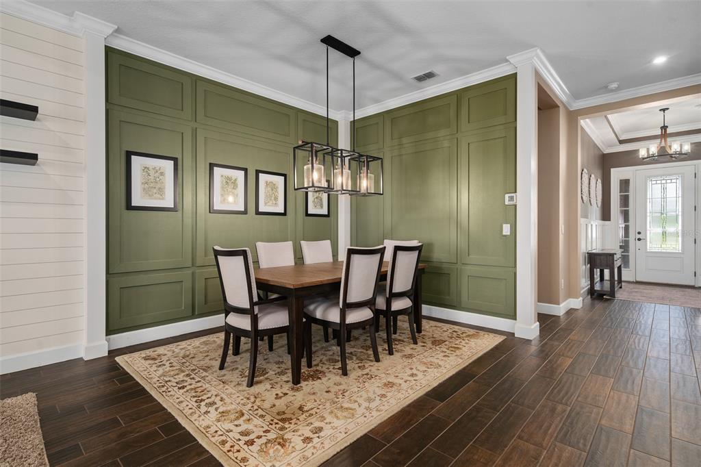 A dining room features olive green paneled walls, a wooden table, and a rectangular chandelier — 1357 ZEEK RIDGE STREET, CLERMONT, FL