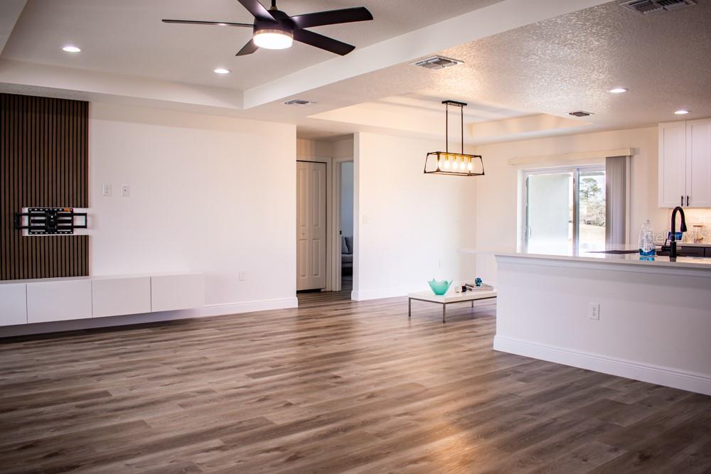 An open-concept living area features wood-look flooring, a slat-wall media console, and a kitchen island — 5104 KIRKWOOD AVENUE, SPRING HILL, FL