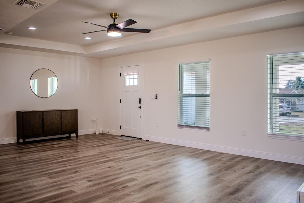 A living room with wood-look flooring, a ceiling fan, a white door, and two windows — 5104 KIRKWOOD AVENUE, SPRING HILL, FL