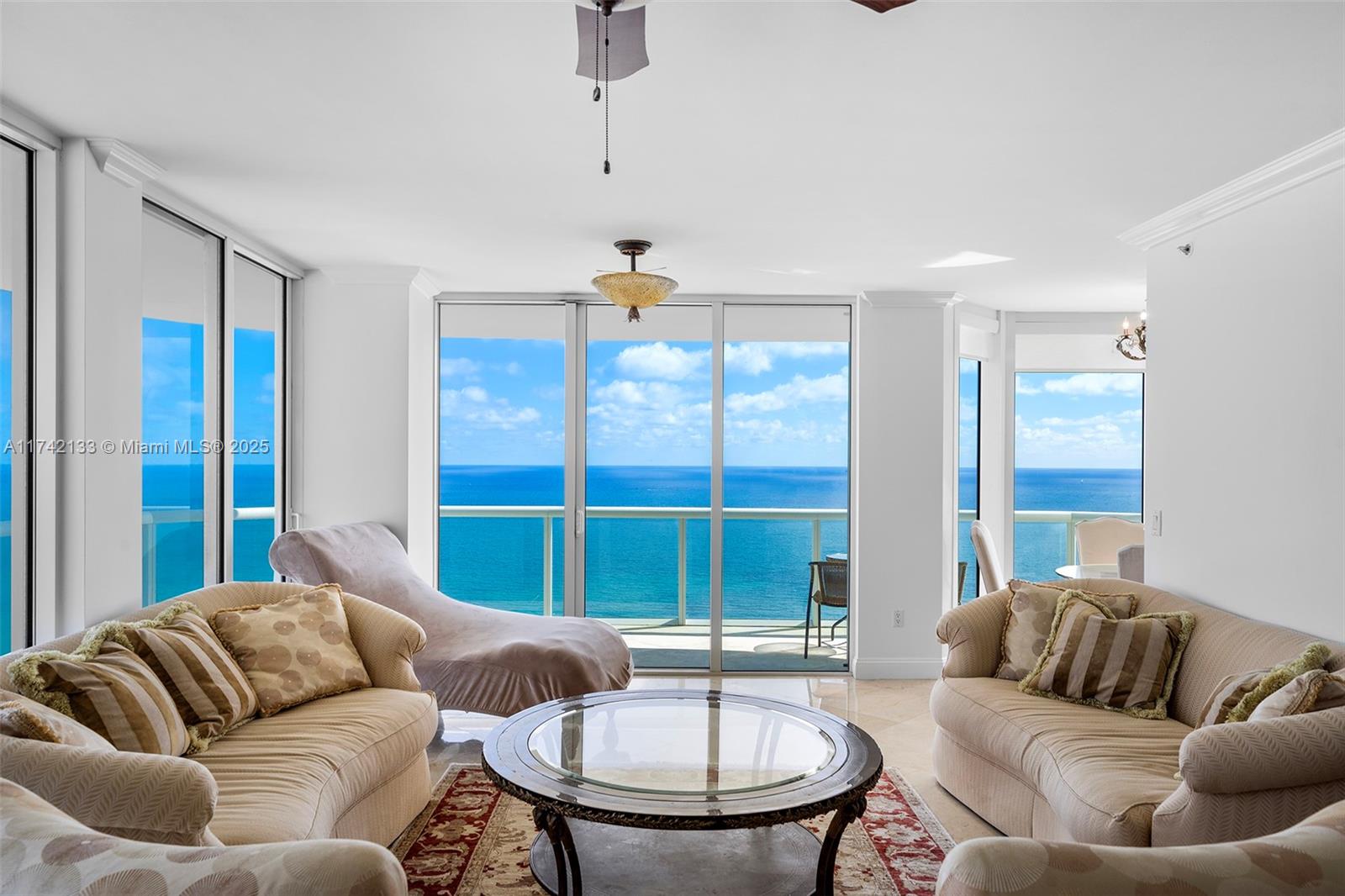 A living room features beige sofas, a glass coffee table, and floor-to-ceiling windows overlooking ocean — 6365 Collins Ave # 3801, Miami Beach FL 33141, MIAMI BEACH, FL