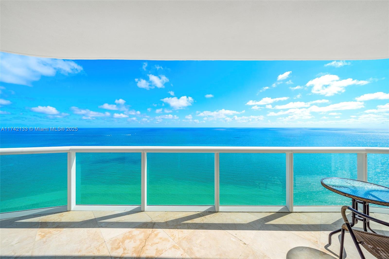 A balcony with a glass railing overlooks the ocean under a bright blue sky — 6365 Collins Ave # 3801, Miami Beach FL 33141, MIAMI BEACH, FL