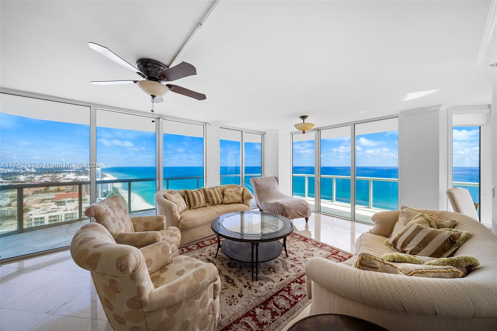 A living room with beige furniture, a patterned rug, and floor-to-ceiling windows overlooking the ocean — 6365 Collins Ave # 3801, Miami Beach FL 33141, MIAMI BEACH, FL