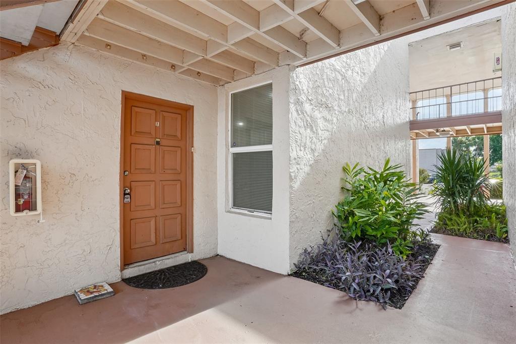 An exterior view of a building entrance with a brown door, window, and small garden — 546 ORANGE DRIVE UNIT 13, ALTAMONTE SPRINGS, FL