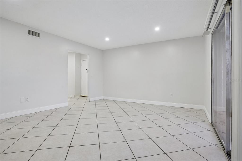 An empty room features light gray walls, white baseboards, tiled flooring, and a sliding glass door — 546 ORANGE DRIVE UNIT 13, ALTAMONTE SPRINGS, FL
