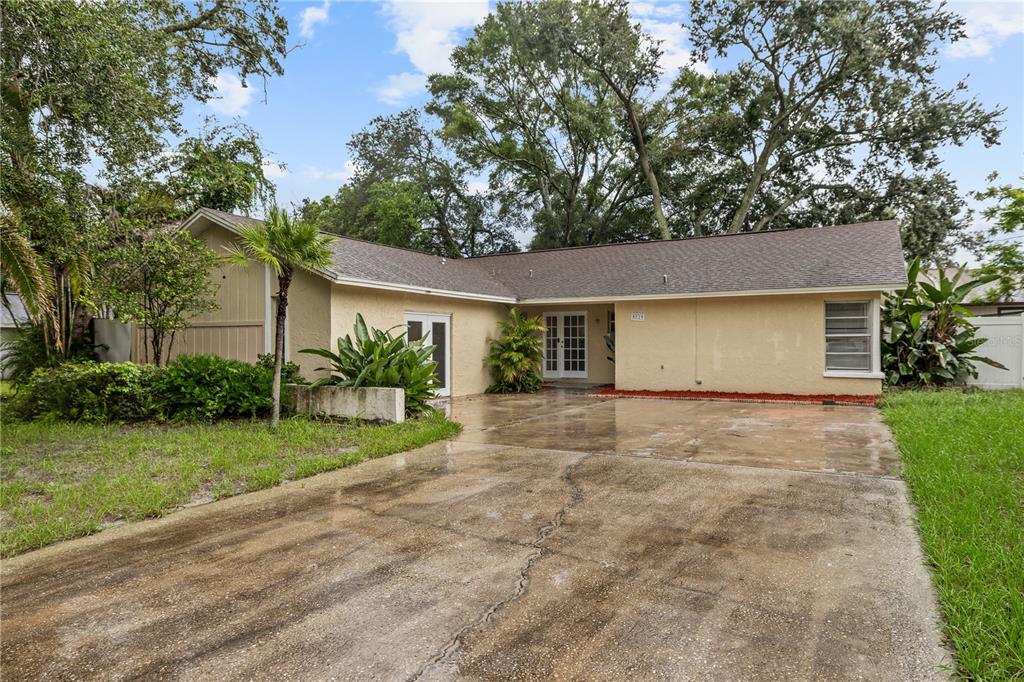 A single-story house with a beige stucco exterior, a concrete driveway, and mature trees — 8529 RENALD BOULEVARD, TEMPLE TERRACE, FL