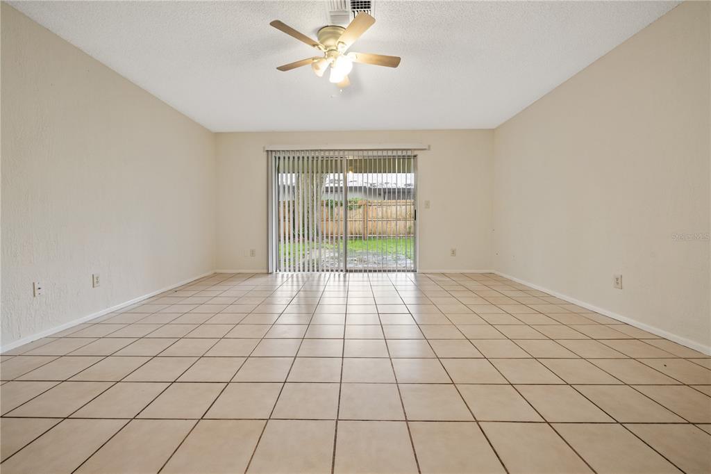 An empty room with beige walls, tile flooring, a ceiling fan, and sliding glass doors — 8529 RENALD BOULEVARD, TEMPLE TERRACE, FL