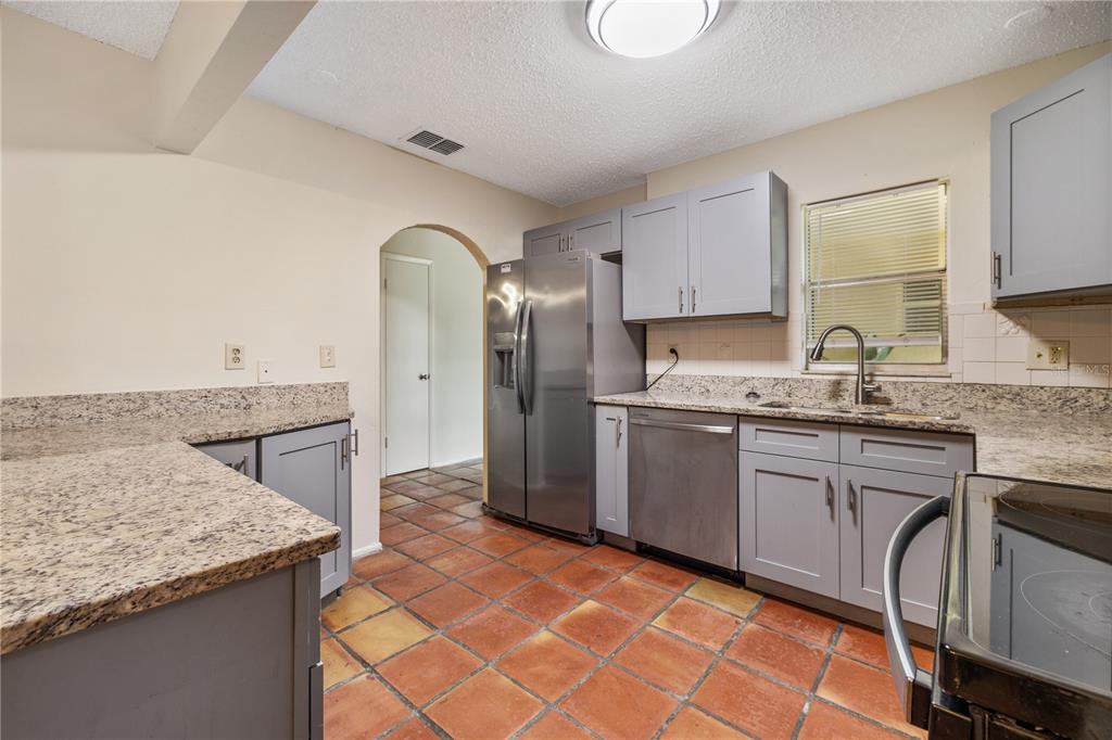 A kitchen features gray cabinets, granite countertops, stainless steel appliances, and terracotta tile flooring — 8529 RENALD BOULEVARD, TEMPLE TERRACE, FL