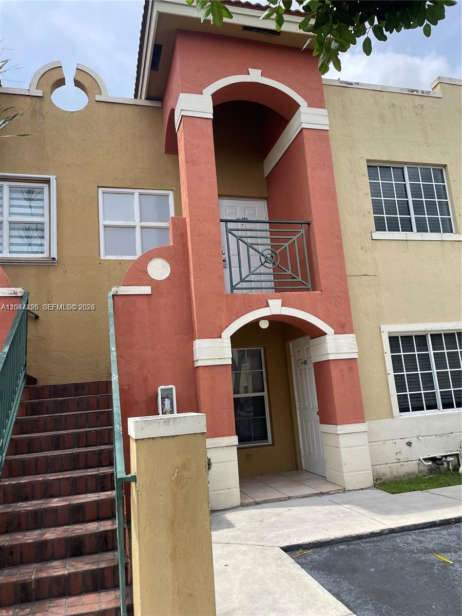 The exterior of a two-story stucco building features a staircase and a small balcony — 15400 SW 134th Pl # 404, Miami FL 33177, MIAMI, FL