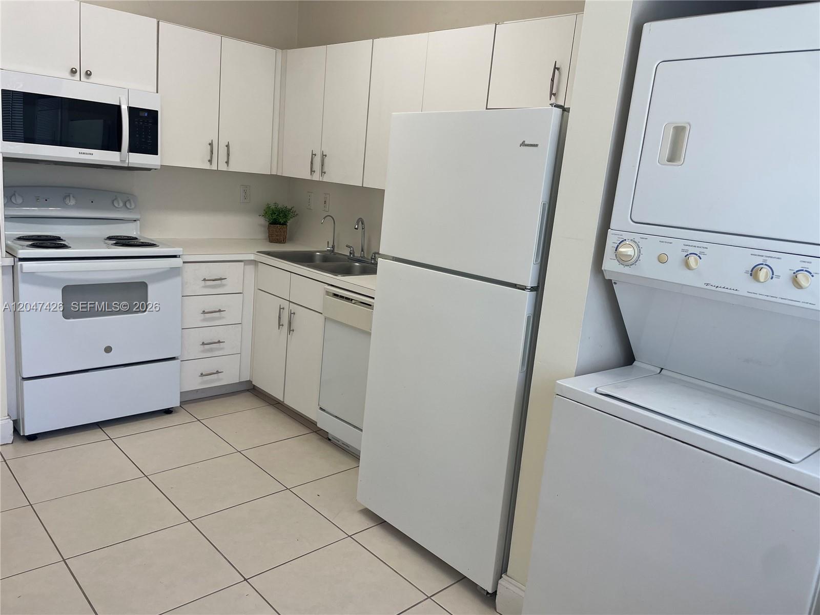 A kitchen features white cabinets, white appliances, a stacked washer-dryer, and light-colored tile flooring — 15400 SW 134th Pl # 404, Miami FL 33177, MIAMI, FL