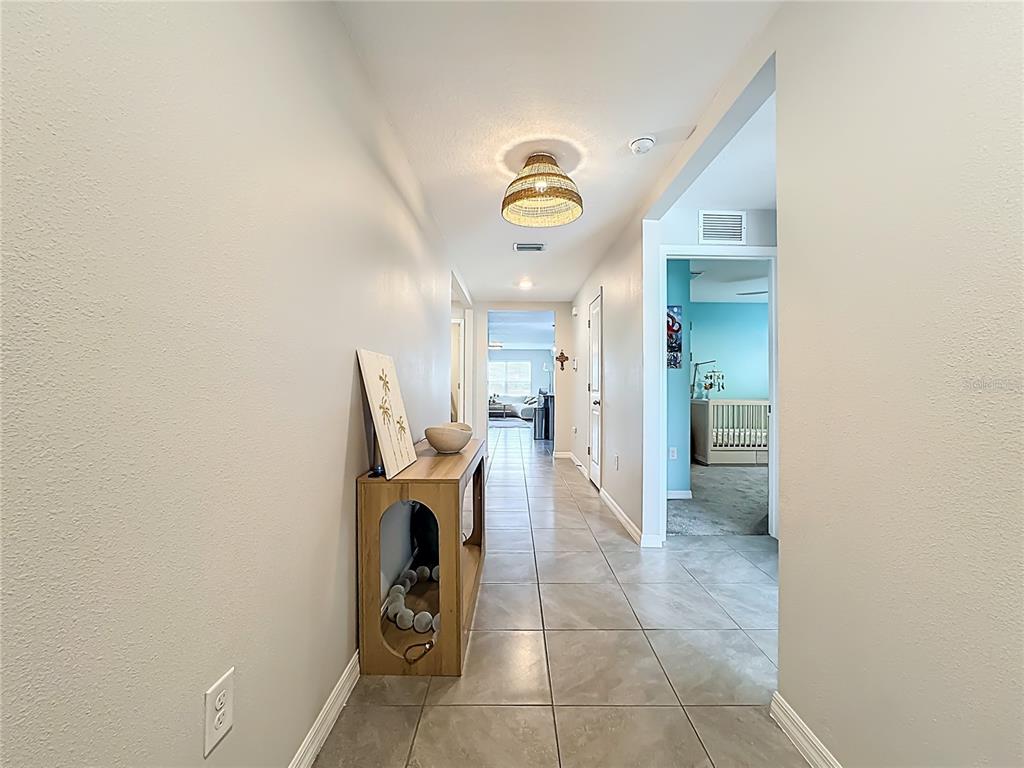 A hallway with light-colored tile flooring leads to a bedroom and a living area — 5209 SONG SPARROW TERRACE, PALMETTO, FL