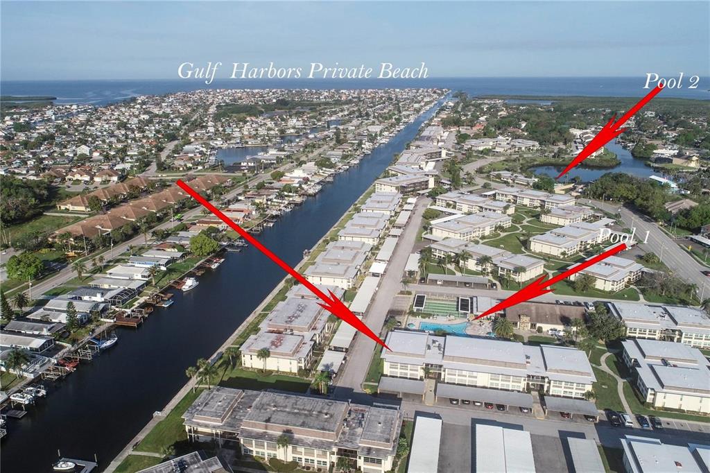An aerial view shows a residential waterfront community with canals, multi-story buildings, and swimming pools — 5111 AMULET DRIVE UNIT 208, NEW PORT RICHEY, FL