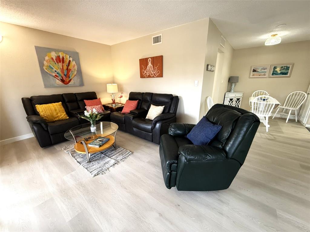 A living room features dark leather furniture, a glass coffee table, and light wood flooring — 5111 AMULET DRIVE UNIT 208, NEW PORT RICHEY, FL