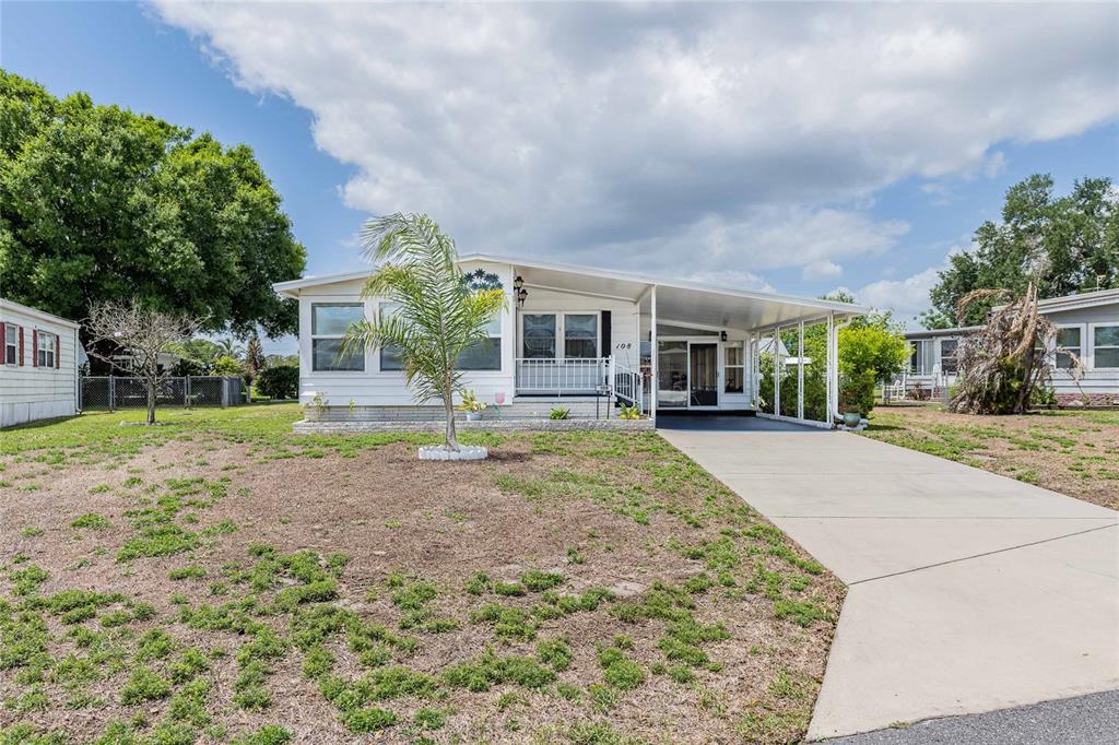 A white single-wide mobile home features a carport, a front porch, and a palm tree — 1610 REYNOLDS RD. UNIT 108, LAKELAND, FL