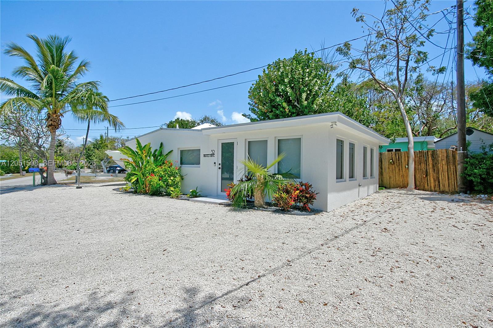 A white, single-story house with a gravel driveway and tropical landscaping under a blue sky — 32 Pirates Dr, Key Largo FL 33037, KEY LARGO, FL
