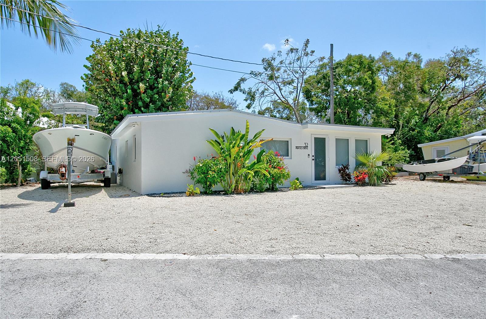 A white single-story house with a gravel yard and two boats parked outside — 32 Pirates Dr, Key Largo FL 33037, KEY LARGO, FL