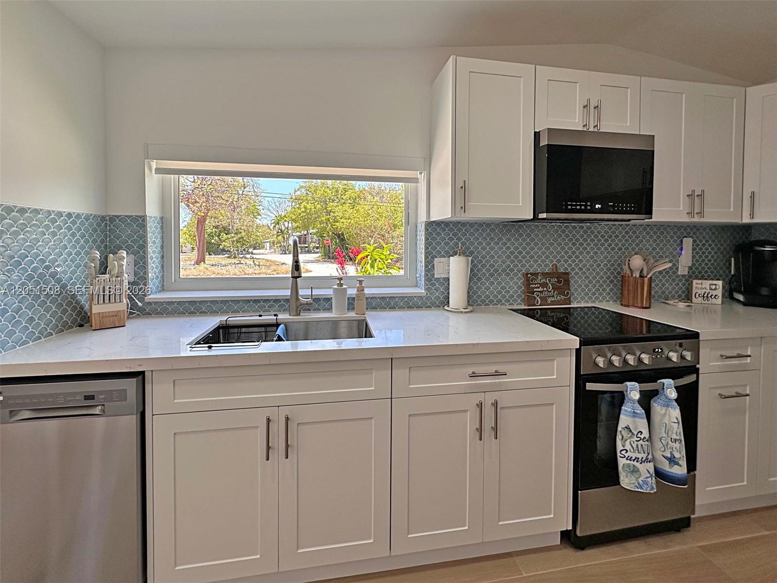 A kitchen features white cabinets, a blue scalloped tile backsplash, and a window above the sink — 32 Pirates Dr, Key Largo FL 33037, KEY LARGO, FL