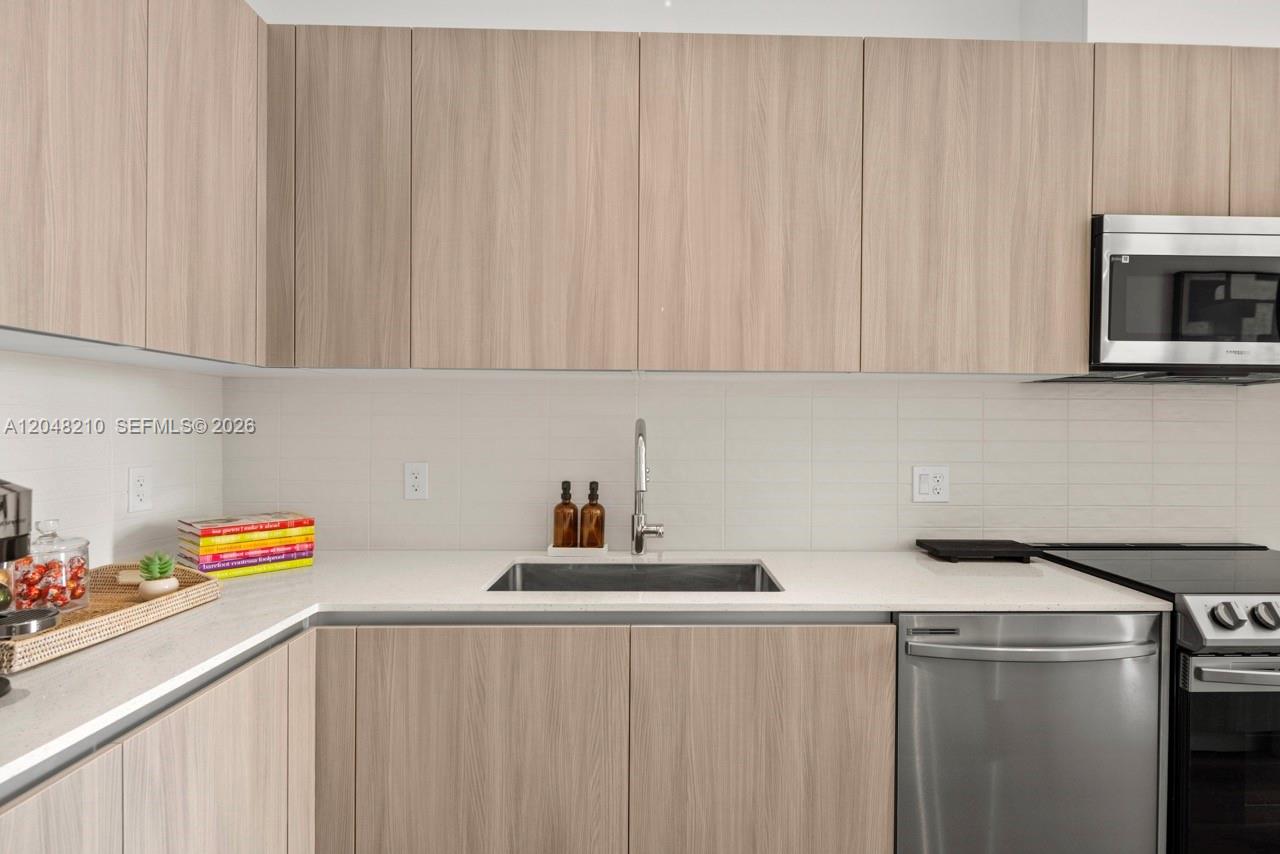 A modern kitchen features light wood cabinets, a stainless steel sink, and stainless steel appliances — 2800 SW 27th Terrace # 0513, Miami FL 33133, MIAMI, FL