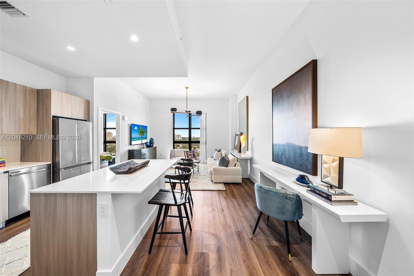 A modern open-concept kitchen and living area features white countertops, wood cabinetry, and hardwood flooring — 2800 SW 27th Terrace # 0513, Miami FL 33133, MIAMI, FL