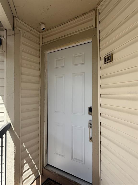 A white front door with a smart lock is set within beige vinyl siding — 1940 LAKE ATRIUMS CIRCLE UNIT 110, ORLANDO, FL