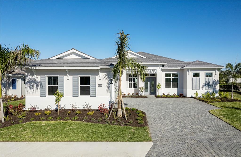 A single-story house with a gray tile roof, white stucco exterior, and a paver driveway — 8065 NEVIS RUN, BRADENTON, FL