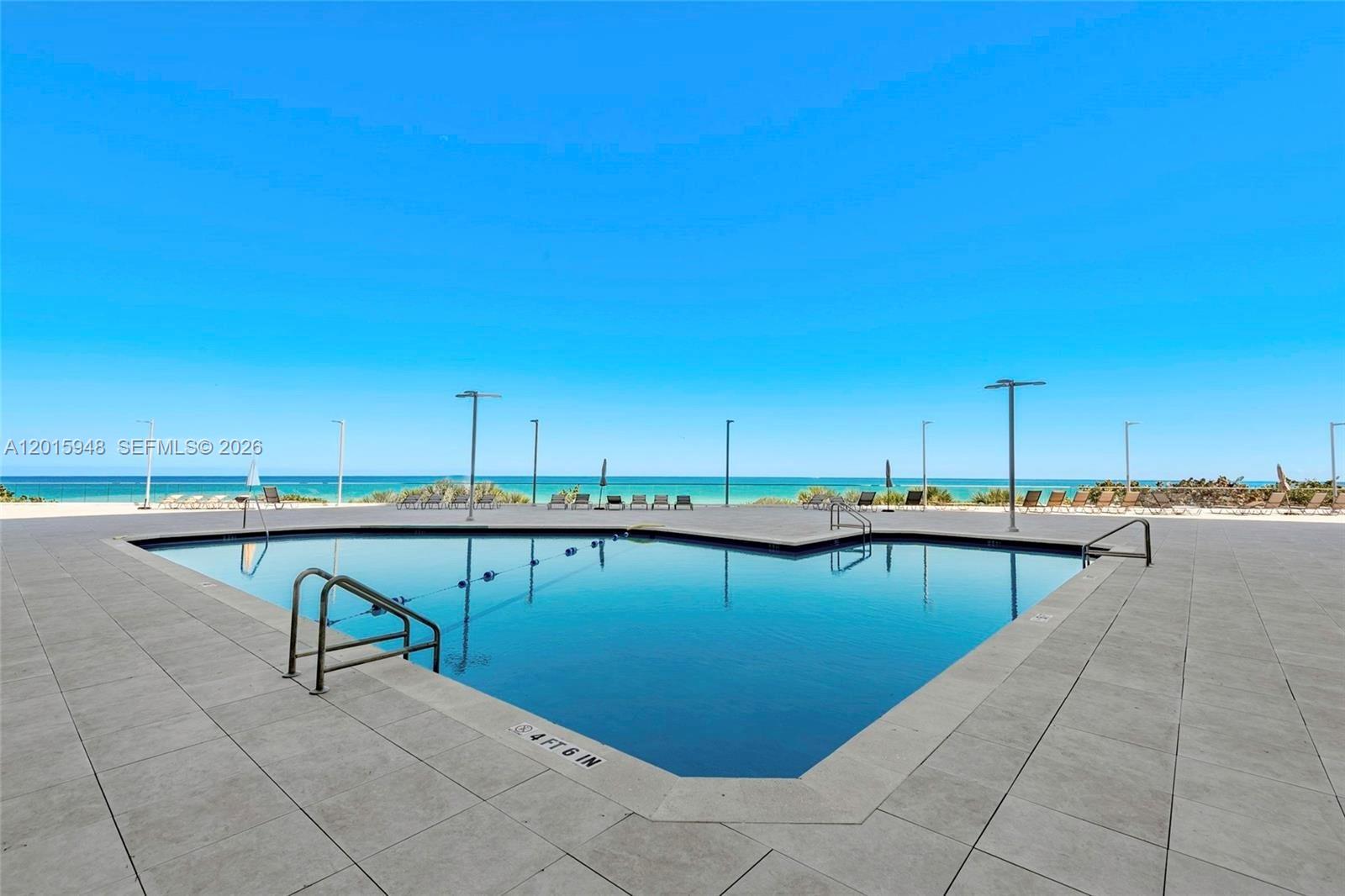 A swimming pool with a depth marker sits on a patio overlooking the ocean — 7135 Collins Ave # 1214, Miami Beach FL 33141, MIAMI BEACH, FL