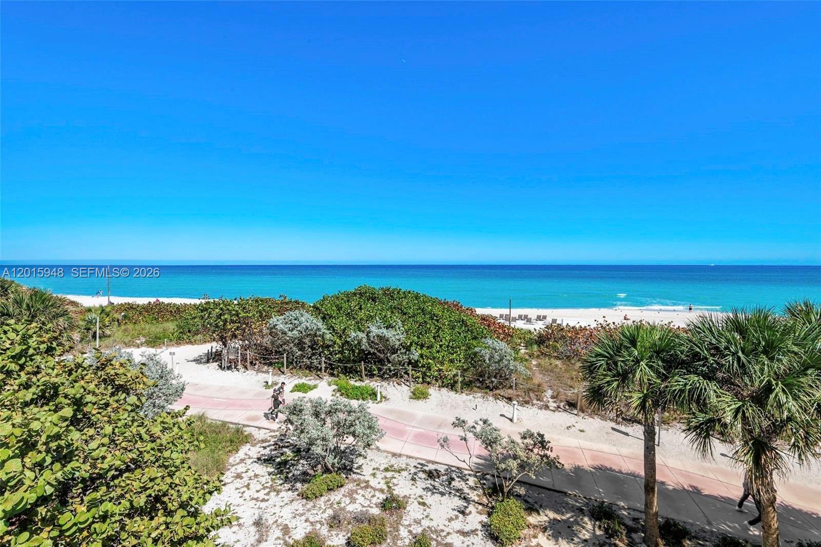 An elevated view shows a paved path winding through coastal vegetation toward a sandy beach — 7135 Collins Ave # 1214, Miami Beach FL 33141, MIAMI BEACH, FL