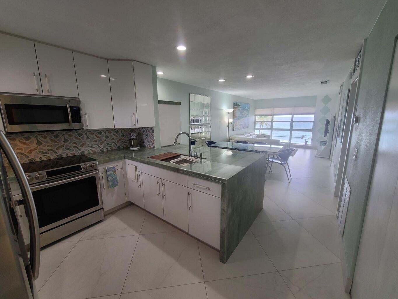 A modern kitchen with white cabinets and a green stone island overlooks an open living area — 3851 N Ocean Boulevard # 409, Gulf Stream FL 33483, GULF STREAM, FL