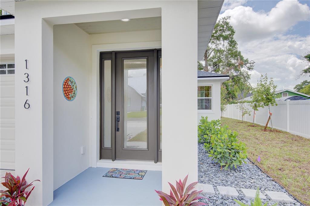 The front entrance of a house features a dark gray door with sidelights and landscaping — 1316 E 9TH AVENUE, MOUNT DORA, FL