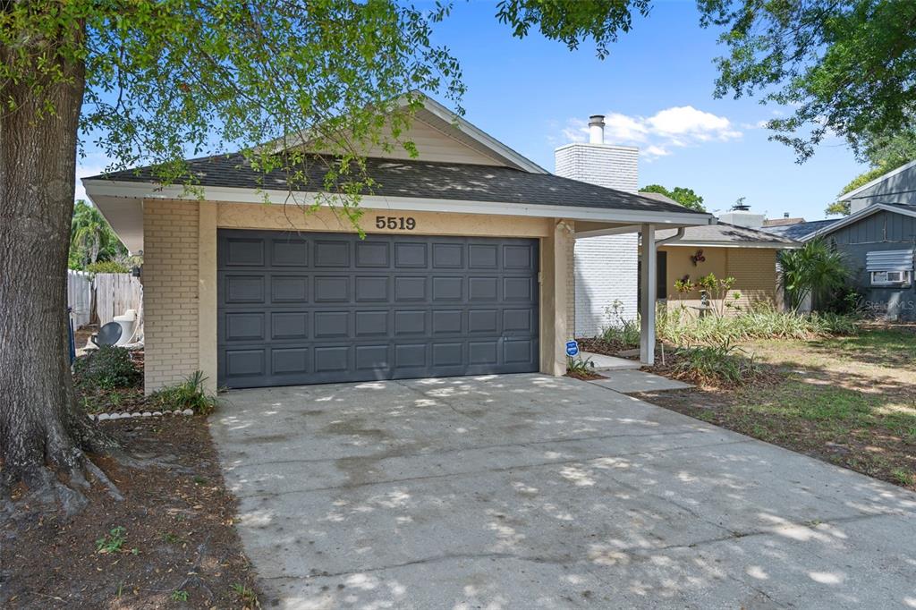 A single-story house with a dark gray garage door, brick exterior, and a concrete driveway — 5519 FULMAR DRIVE, TAMPA, FL