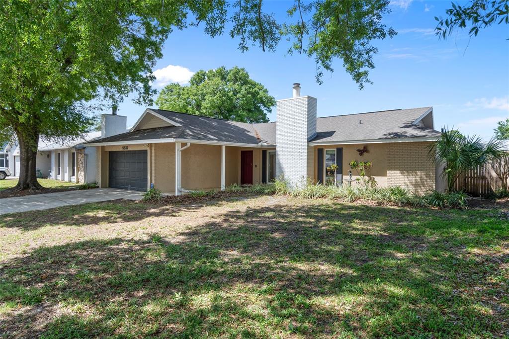 A single-story house with a brick chimney, tan stucco walls, and a two-car garage — 5519 FULMAR DRIVE, TAMPA, FL